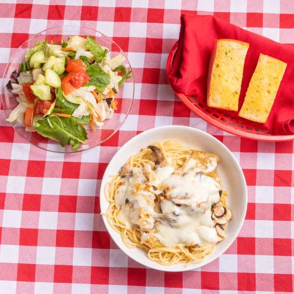 Spaghetti with creamy mushroom sauce, a side salad, and garlic bread on a red and white checkered tablecloth.