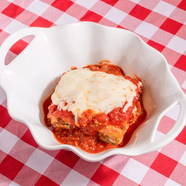 A serving of lasagna with melted cheese and red sauce in a white dish on a red and white checkered tablecloth.