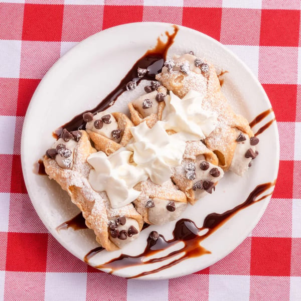 A plate of cannoli, drizzled with chocolate sauce, topped with whipped cream and chocolate chips.