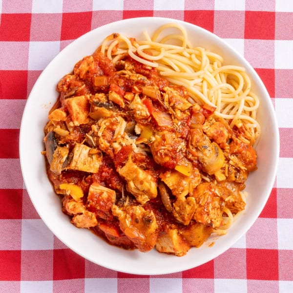 Spaghetti with chicken cacciatore in a white bowl on a red and white checkered tablecloth.