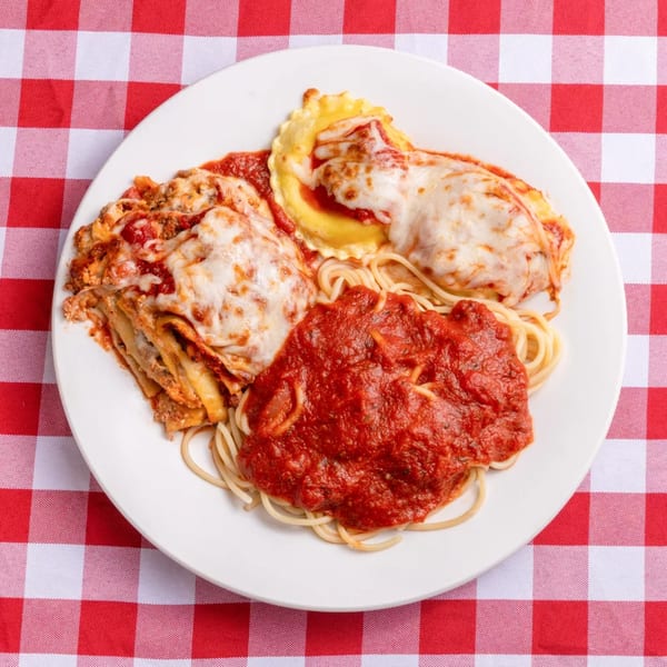 A white plate with lasagna, ravioli, and spaghetti with red sauce on a red and white checkered tablecloth.