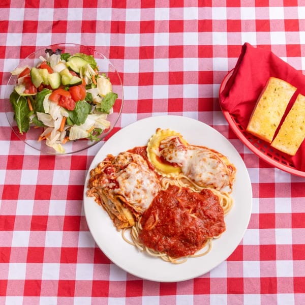 Italian dinner with lasagna, ravioli, spaghetti, salad, and garlic bread on a red and white checkered tablecloth.
