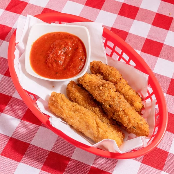 Golden-brown mozzarella sticks in a red basket with a side of marinara sauce on a red and white checkered tablecloth.
